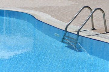 Ladder to the outdoor pool with blue transparent water.