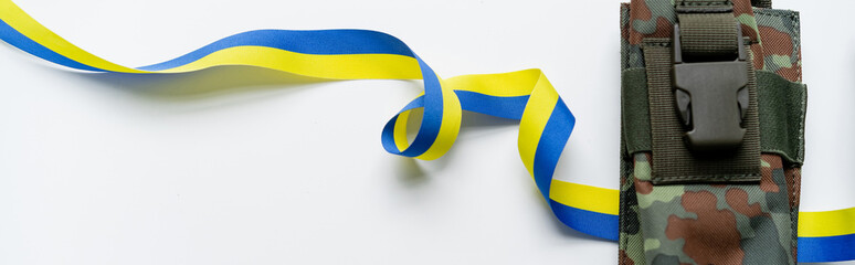 Top view of blue and yellow ribbon near military bag on white background, banner.