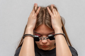 A young girl handcuffed on a gray background, close-up. Juvenile delinquent in a black T-shirt,...