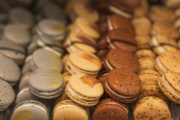 A lot of beautiful French sweets macarons of yellow brown chocolate colors lie in rows in assortment in a bakery