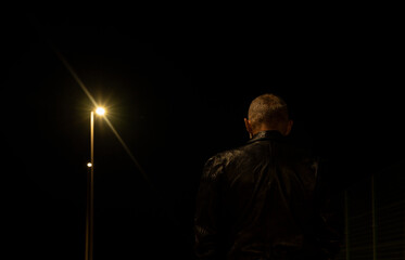 Rear view of adult man walking on street at night with lights of street lamps