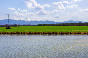 Reflections of the sun in the water of the blue lake in a green landscape with snowy mountains, La Pinilla Spain.