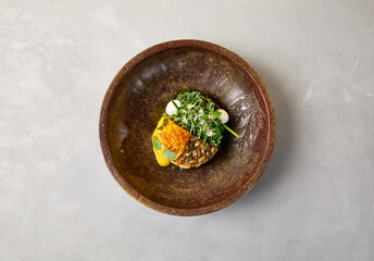 Pumpkin steak with chicken and spinach on dark ceramic plate. Healthy food in modern dishware. Innovative recipes in contemporary style. Roasted turkey with pumpkin on gray concrete background.