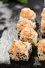 Baked Maki sushi on dark slate. Hot sushi roll with salmon and cheese. Sushi roll sesame outside, baked salmon and cheese topped. Style concept japanese menu with black background, leaves and shadow.