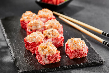 Baked Maki sushi on dark slate. Hot sushi roll with salmon. Sushi roll with tobiko outside, baked fish  and cheese topped. Style concept japanese menu with black background, leaves and hard shadow.