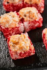Baked Maki sushi on dark slate. Hot sushi roll with salmon. Sushi roll with tobiko outside, baked fish  and cheese topped. Style concept japanese menu with black background, leaves and hard shadow.