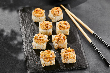 Baked Maki sushi on dark slate. Hot unagi maki with eel. Sushi roll with baked eel, cheese and unagi sauce topped. Style concept japanese menu with black background, leaves and hard shadow.