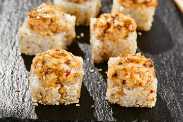 Baked Maki sushi on dark slate. Hot unagi maki with eel. Sushi roll with baked eel, cheese and unagi sauce topped. Style concept japanese menu with black background, leaves and hard shadow.