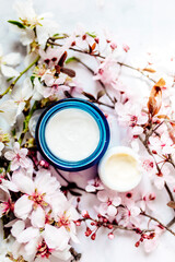 Obraz na płótnie Canvas Top view of cosmetic cream and concealer eyes creams with pink cherry flowers in a blue glass jar. Hygienic skincare lotion product. Vertical photo