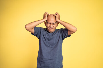 Stressed asian bald young man holding head on isolated background