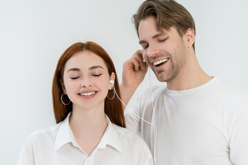 Cheerful young couple listening music in earphones isolated on white.