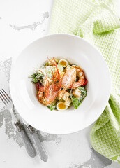 Classic Caesar salad with shrimps in white plate on stone table. Italian menu in restaurant. Seafood caesar on rustic style. Trendy salad with grilled prawns, green leaves, eggs, croutons and cheese.