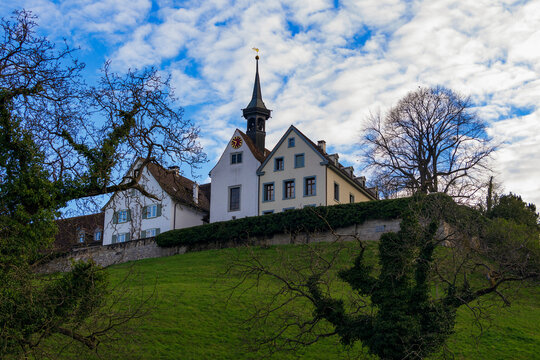 Panoramic view of St Margaret's Church in Binningen standing on a high hill covered in green grass against a blue cloudy sky. Baroque reformed church building with chapel and bell tower