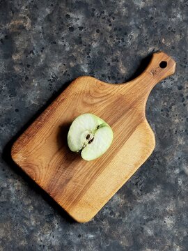 Slice of green apple on wooden cutting board on black concrete background with copy space. Granny smith. Spring fruits background.
