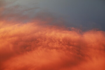 Dramatic sunset landscape with puffy clouds lit by orange setting sun and blue sky.