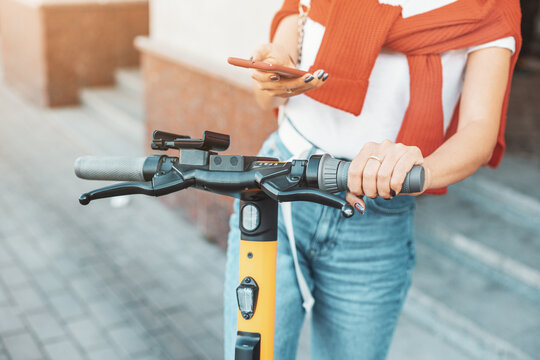 A student girl rents an electric scooter and unlocks it using an app on her smartphone. Sharing economy and modern urban transport