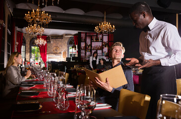 Fototapeta na wymiar Portrait of young man holding menu and ordering food in luxury restaurant
