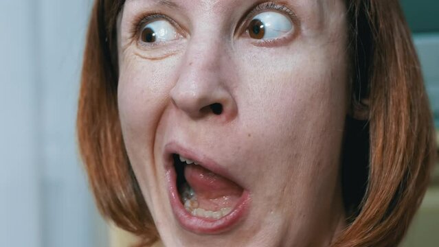 Close-up Facial Expressions of a Crazy Woman with Bulging Eyes, Crooked Teeth. A woman with wrinkles on face looks at the camera, makes a face, grimaces, moves lips, rotates eyes wide open. Behavior.