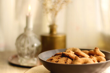Bowl of sugar cookies and chocolate chip cookies, lit candle and vase with flowers on the table. Selective focus.