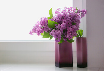 Lilac flowers in a vase stand on a white window. Beautiful branches of lilac flowers on a white background, natural spring background, soft selective focus, copy space