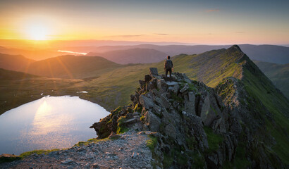 Hiker surveying the summit of Helvellyn at sunrise, with first light illuminating the rugged...