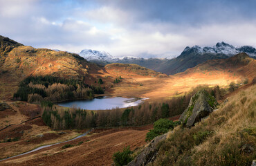 Atmospheric and dramatic light across a valley of the Lake District in winter, with snow on the tops of the mountains