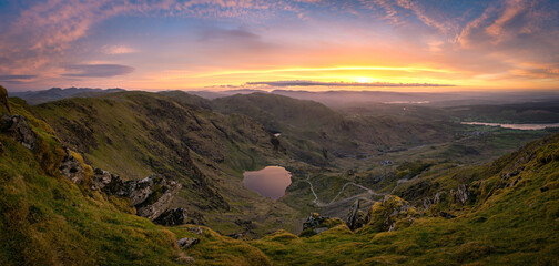 Panorama from the summit of the Old Man of Coniston, with a fiery stunning sunrise and a view down to the tarn 