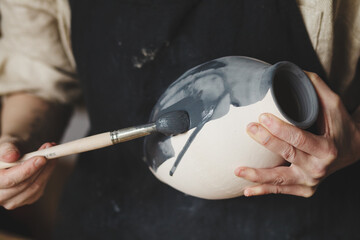 Young female potter glazing clay vase, traditional pottery making - obrazy, fototapety, plakaty
