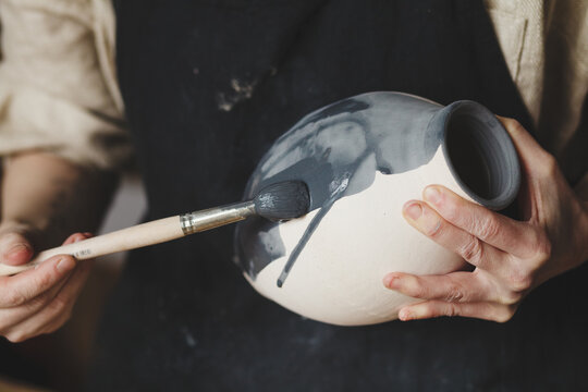 Young female potter glazing clay vase, traditional pottery making