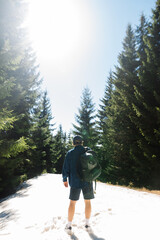 Obraz premium Male hiker in casual clothes standing in the mountains in the snow in the woods on a sunny day, view from the back.