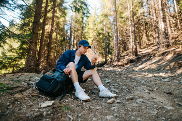 Handsome young male tourist in casual clothes sitting on a mountain trail and using a smartphone with a serious face.