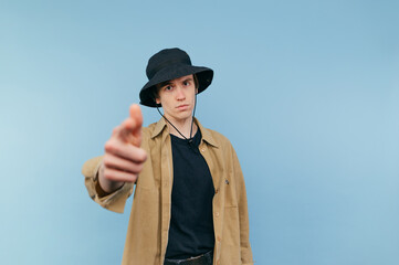 handsome young man in panama and shirt stands on a blue background and with a serious face shows...