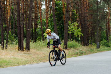 Naklejka premium Handsome young male cyclist trains outside the city in the woods on the road. Riding a bike.