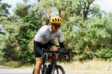 Naklejka premium Positive young male cyclist in sportswear rides a bicycle outside the city in the woods and looks away with a smile on his face.