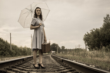 A young fashionista woman in vintage style with a suitcase and a summer umbrella stands on the...