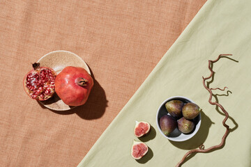 Directly above view of fresh pomegranates on small plate and figs in bowl placed on different tableclothes