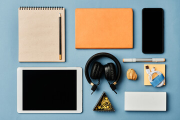 Directly above view of modern devices, notepads, power band, cord and pins on blue background