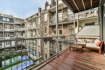 A spacious balcony with wooden floors and furniture with a seating area and a view of the courtyard...