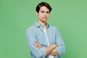 Tired fatigued displeased unnerved tired gloomy young brunet man 20s years old wear blue shirt hold hands crossed isolated on plain green background studio portrait. People emotions lifestyle concept
