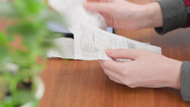 A woman looks through receipts for purchases. Hands close-up. Home Accounting and Investments.