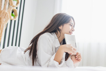 Portrait young smile happy beautiful asian woman relax bedroom.  Young womanl reading book in morning