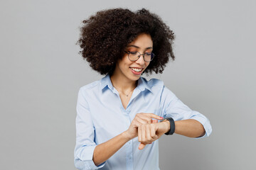 Young smiling happy fun employee business corporate lawyer woman of African American ethnicity in classic formal shirt work in office use look at smart watch isolated on grey color background studio.