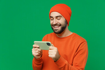 Young gambling happy cool man 20s wear orange sweatshirt hat using play racing app on mobile cell...