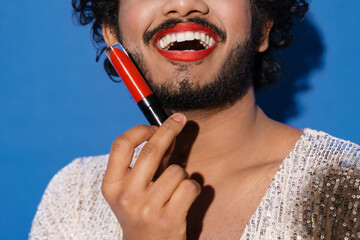 Young curly man with makeup smiling and showing lipstick