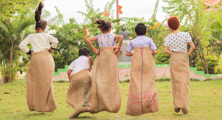 back view shot of Group of Childrens playing potato sack jumping race game at park during summer camp - concept of childhood physical activities and holiday nations. - Powered by Adobe