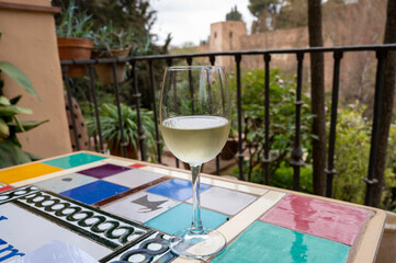 Glass of Spanish dry white wine served on outdoor terrace with view on red walls of Andalusian fortress Alhambra in Granada, Spain