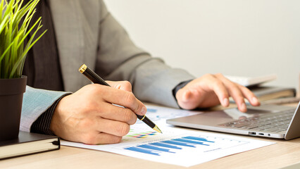 Businessman with pen pointing to graph, financial data, research, develop, market report. Strategic planning, analyzing, calculating financial accounts with calculator and laptop in the office.