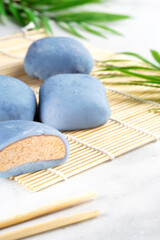 Fototapeta na wymiar A Japanese rice cake lying on a wooden mat on white countertop. Concept of a traditional Japanese mochi with a maki sudare mat and chopsticks on the table. Asian dessert, mochi ice cream, Asian food
