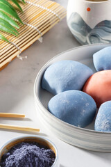 Concept of a traditional Japanese dessert. A ceramic bowl of Japanese mochi with chopsticks and maki sudare mat on white countertop. Asian rice cake, mochi ice cream, Asian sweet street food.