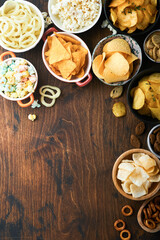 Unhealthy food or snacks. All classic potato snacks with peanuts, popcorn and onion rings and salted pretzels in bowl plates on old wooden background. Unhealthy food for figure, heart, skin, teeth.